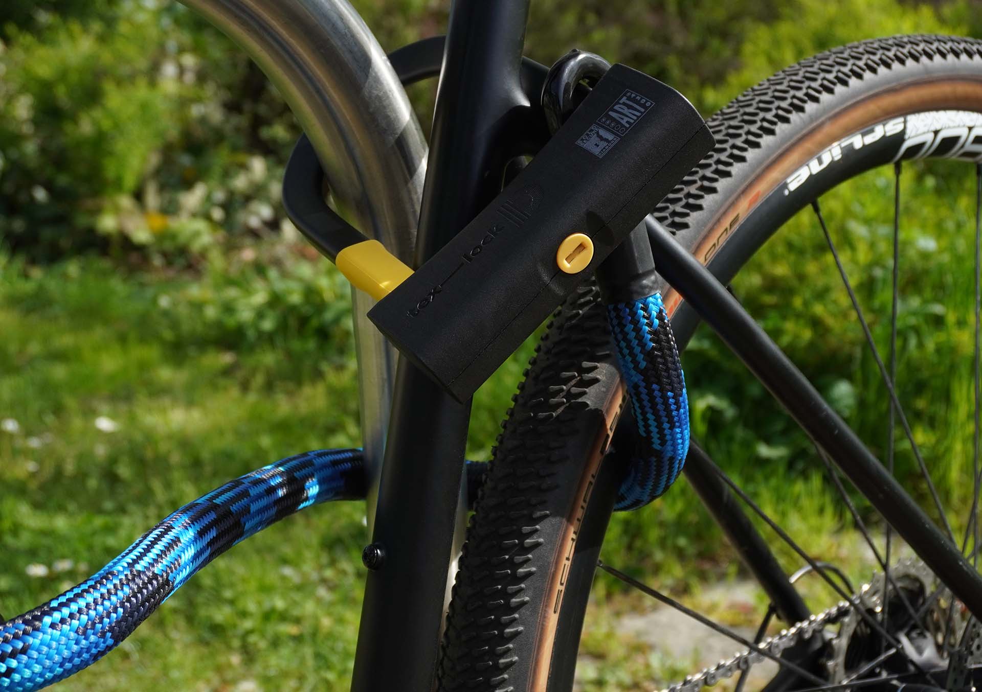 D-lock Bügelschloss sichert Fahrrad an Sattelstande und Sattelstrebe mit Textilseil in morpho blue an Fahrradständer