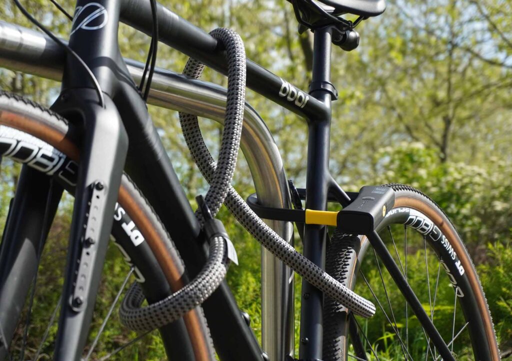 Fahrrad am Hinterrad, Vorderrad und Fahrradrahmen mit D-lock Bügelschloss und eyelet-Textilseil in electric grey am Fahrradständer angeschlossen