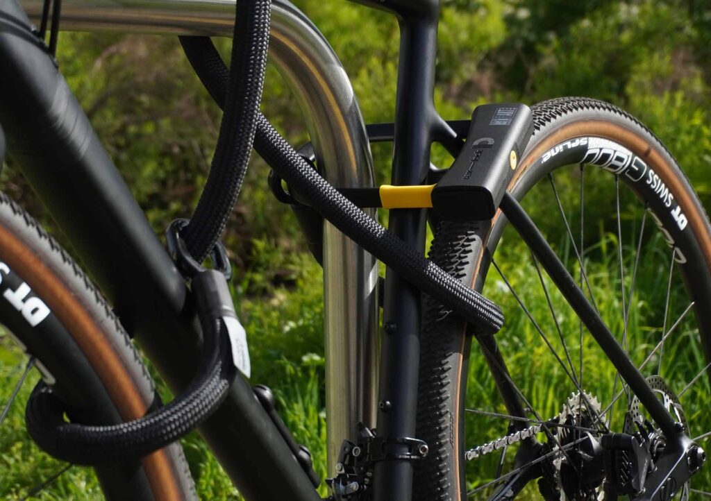 Fahrrad am Hinterrad, Vorderrad und Fahrradrahmen mit D-lock Bügelschloss und eyelet-Textilseil in onyx black am Fahrradständer angeschlossen