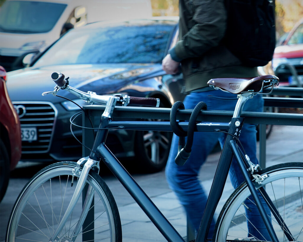 Textiles Seilschloss tex-lock orbit in schwarz sichert Fahrradrahmen an Fahrradständer an einer Straße