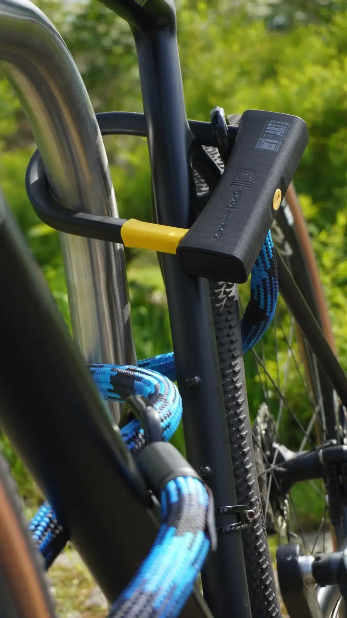 Fahrradrahmen und Hinterrad mit tex–lock eyelet-Textilseil in morpho blue und D-lock Bügelschloss an Fahrradständer angeschlossen