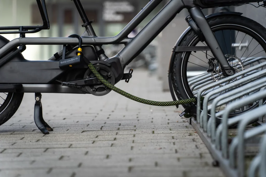 Bügelschloss mit Textilseil in schwarz-neongelben Muster schließt Longtail-Bike an Fahrradständer an