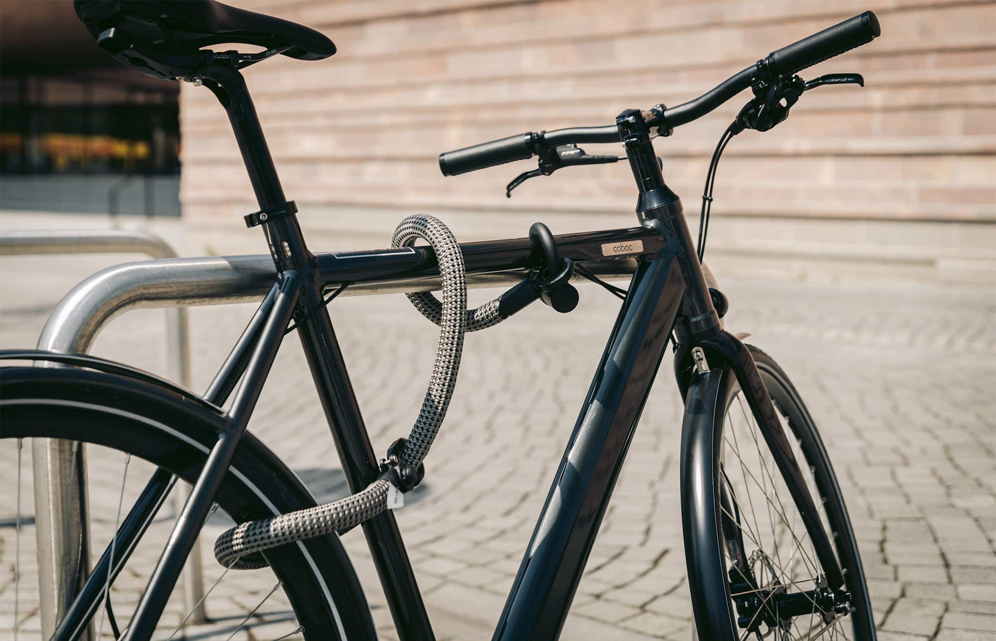 schwarz-graues texlock eyelet Set Textilschloss sichert mehrere Fahrradteile am Fahrradständer
